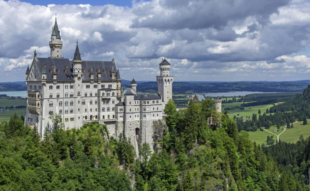 Stunning view of Neuschwanstein Castle surrounded by lush green forests and clouds.